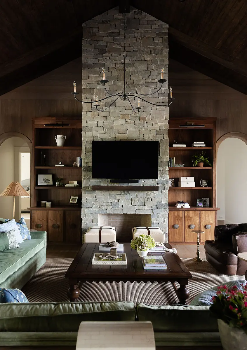 Living room with stone fireplace, green sofa, brown chair, wooden coffee table, and wall-mounted television.