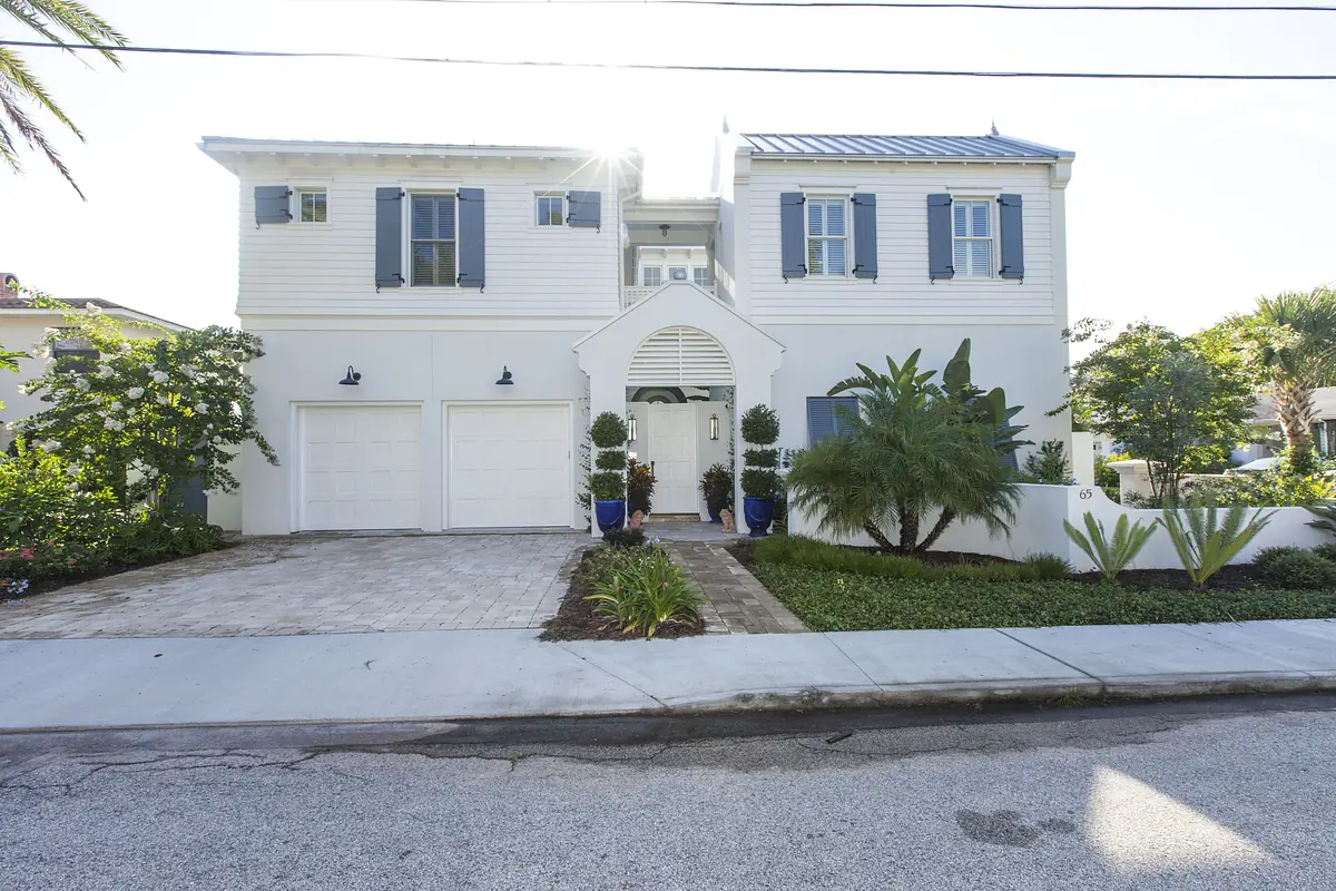 Exterior front view of a house with white siding, blue shutters, garage doors, paved driveway, and landscaping.