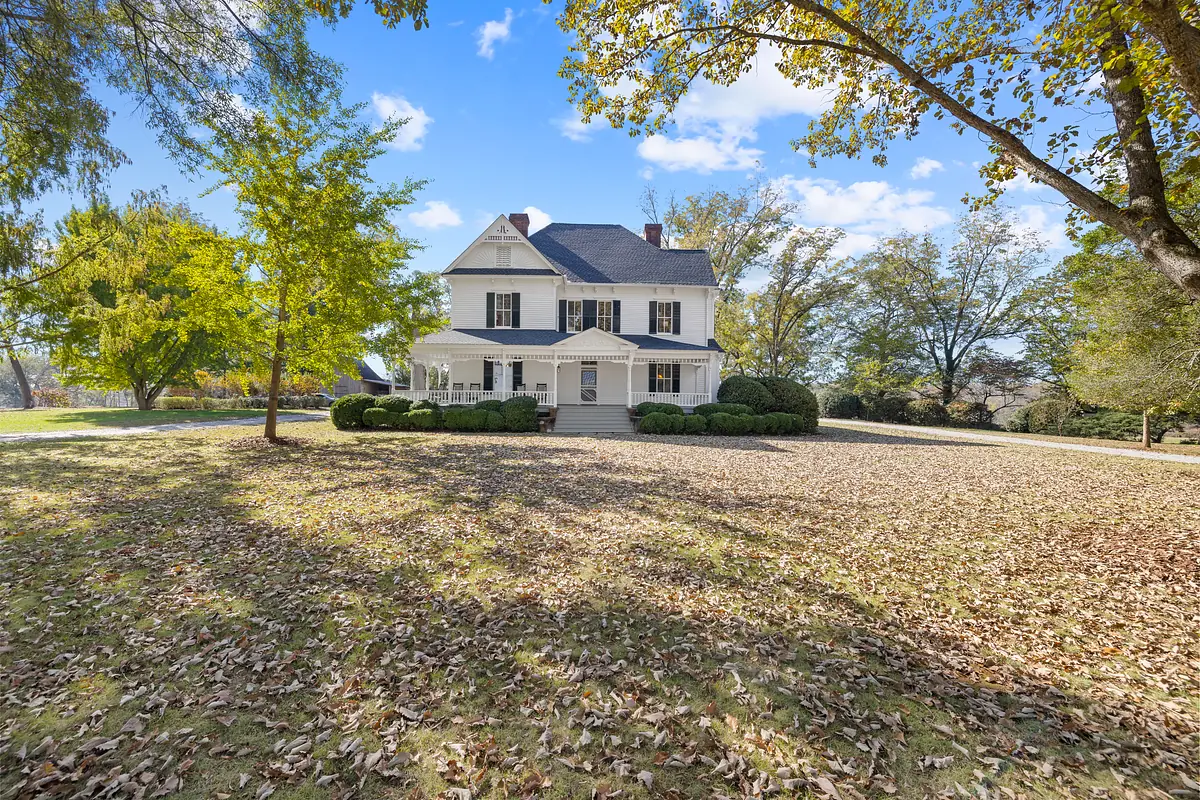 Exterior front of a two-story white house with porch, surrounded by trees and fallen leaves.