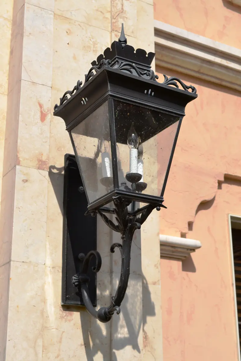 Outdoor wall-mounted lantern in black metal with glass enclosure and decorative detailing.