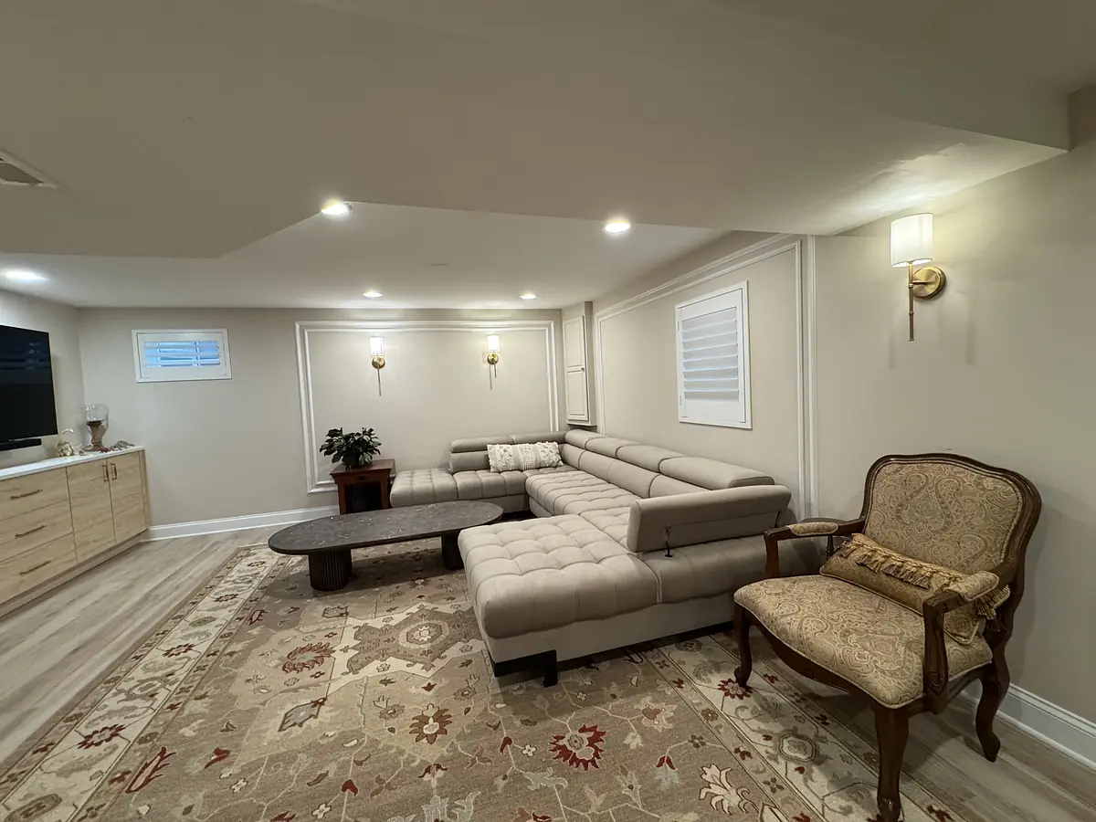 Living room with sectional sofa, coffee table, armchair, area rug, windows, and television cabinet.