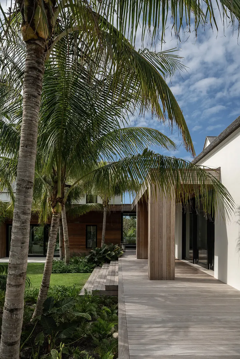 Exterior front with wooden deck, palm trees, and landscaped greenery beside a modern structure.