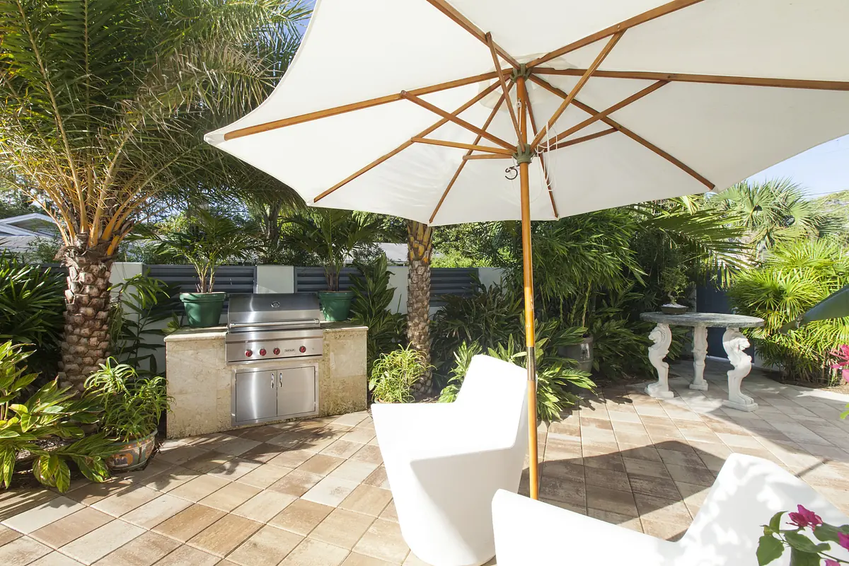 Patio with grill, round table, two white chairs, and numerous palm plants with large tiles floor