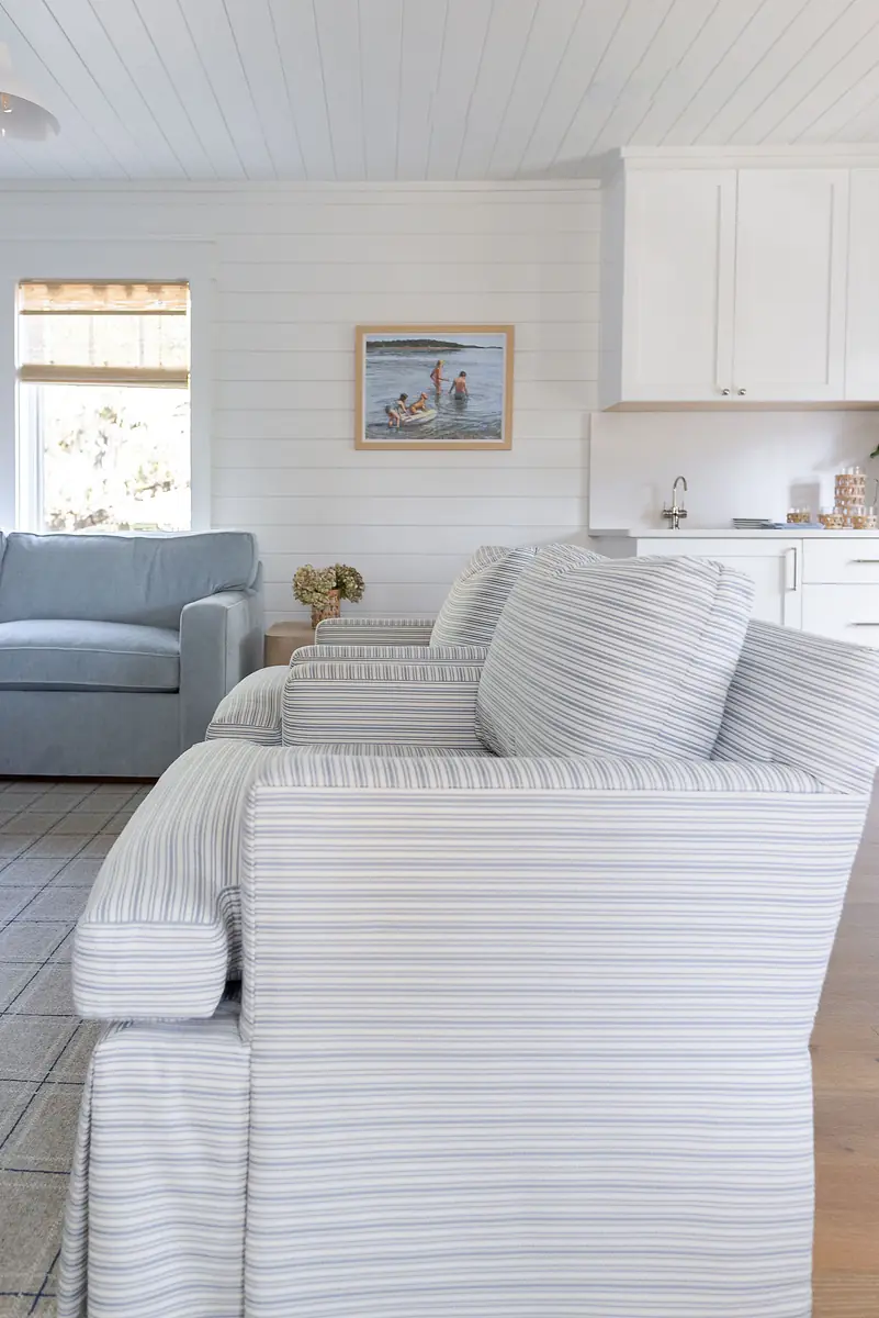 Living room with striped chairs, blue sofa, framed painting, window, and wood flooring.