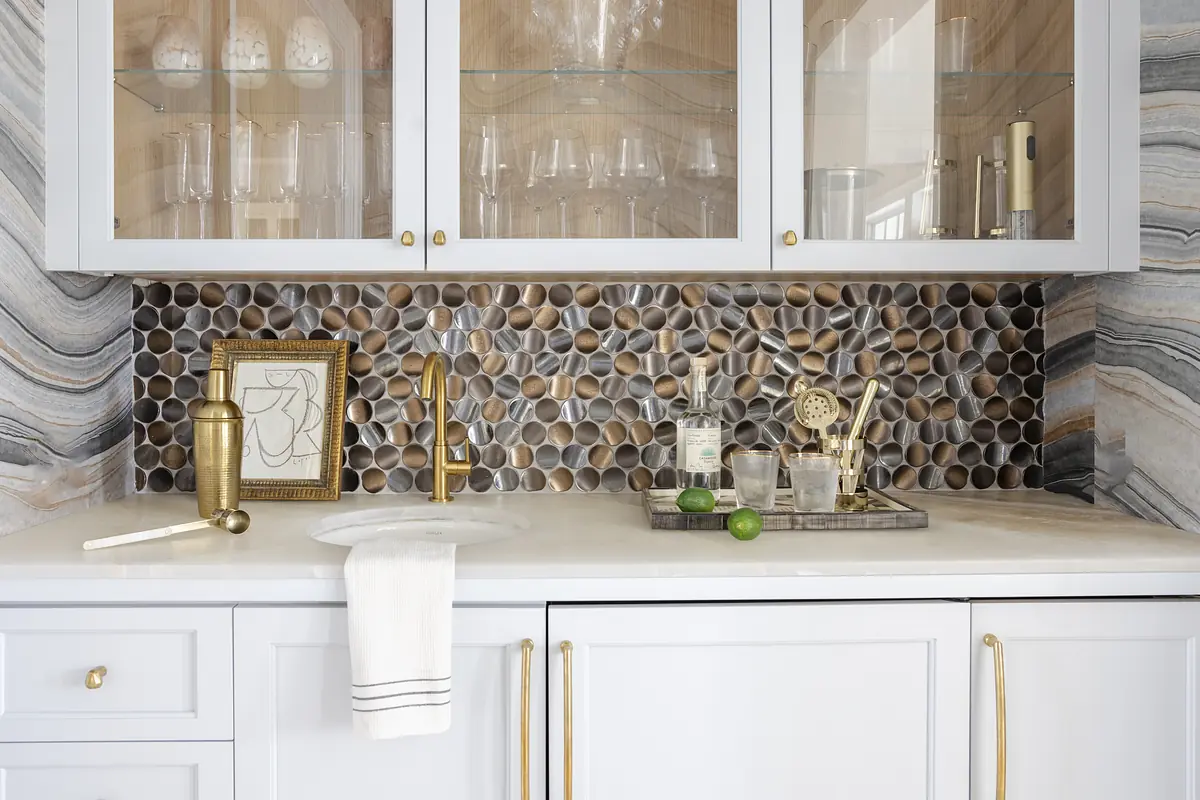 Kitchen countertop with white cabinets, sink, pebble stone backsplash, and kitchen accessories on a tray.