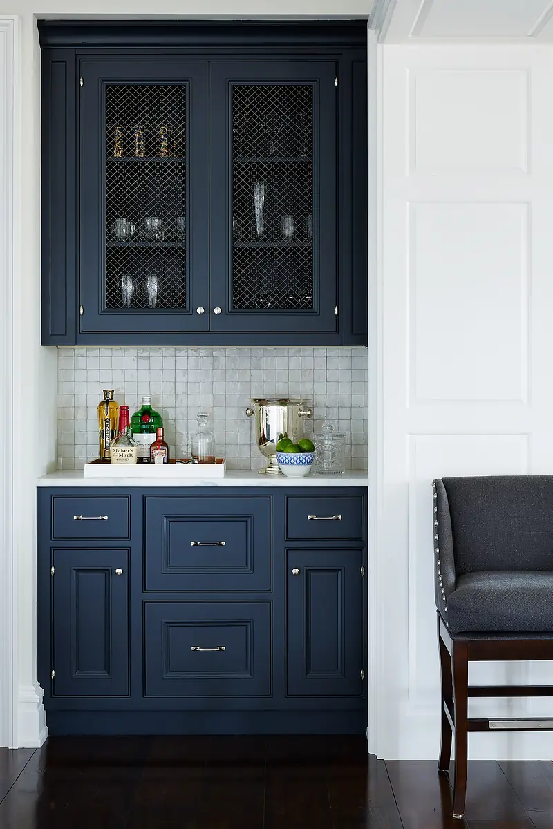 Butler's pantry with dark blue cabinetry, white countertops, sink, tiled backsplash, and bar stool.