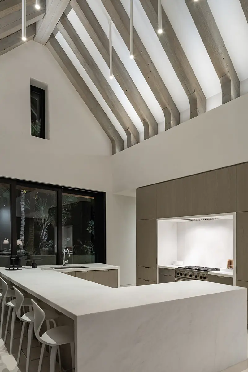 Kitchen with white marble island, beige cabinetry, stainless steel stove, and wooden beam ceiling.