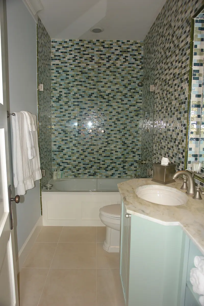 Bathroom with bathtub, tiled backsplash, marble vanity, and light-colored tiles.