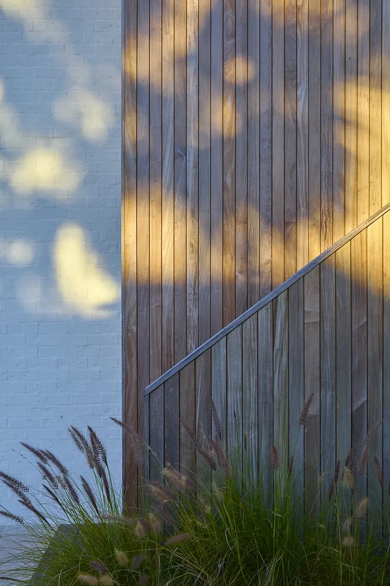 Exterior front view with wood paneling, white brick, grass, ornamental plants, and metal railing leading up.