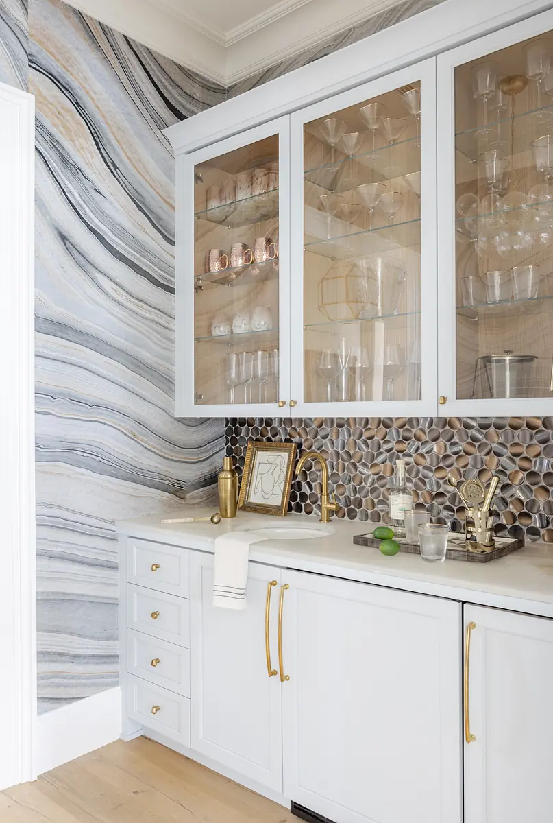 Butler's pantry with white cabinetry, marble countertop, pebble stone backsplash, and wavy marble wall.