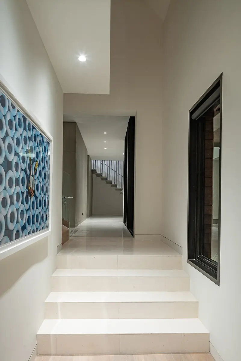 Hallway with white stairs, circular artwork, light walls, and floor-to-ceiling windows for natural light