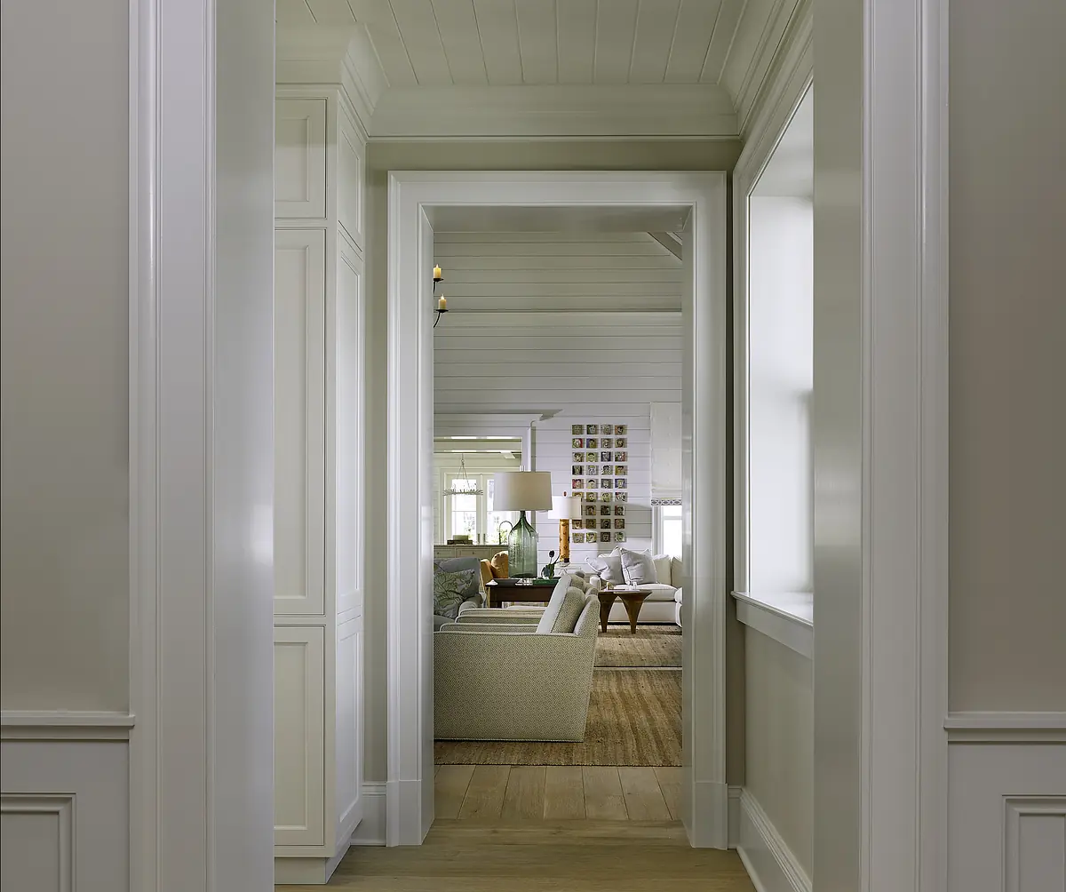 Hallway with paneled walls and archway leading to a living room with green sofa and wood coffee table.