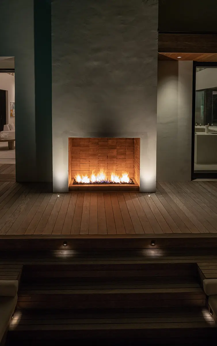 Exterior rear area with built-in wood fireplace, wooden decking, and steps leading up with recessed lighting.