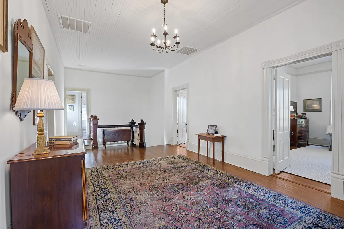 Hallway with patterned rug, wooden console table, chandelier, and two doors to adjacent rooms.