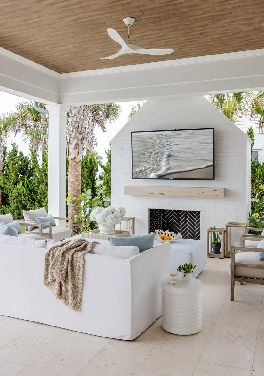 Patio with white sectional sofa, side table, TV above fireplace, and surrounding greenery
