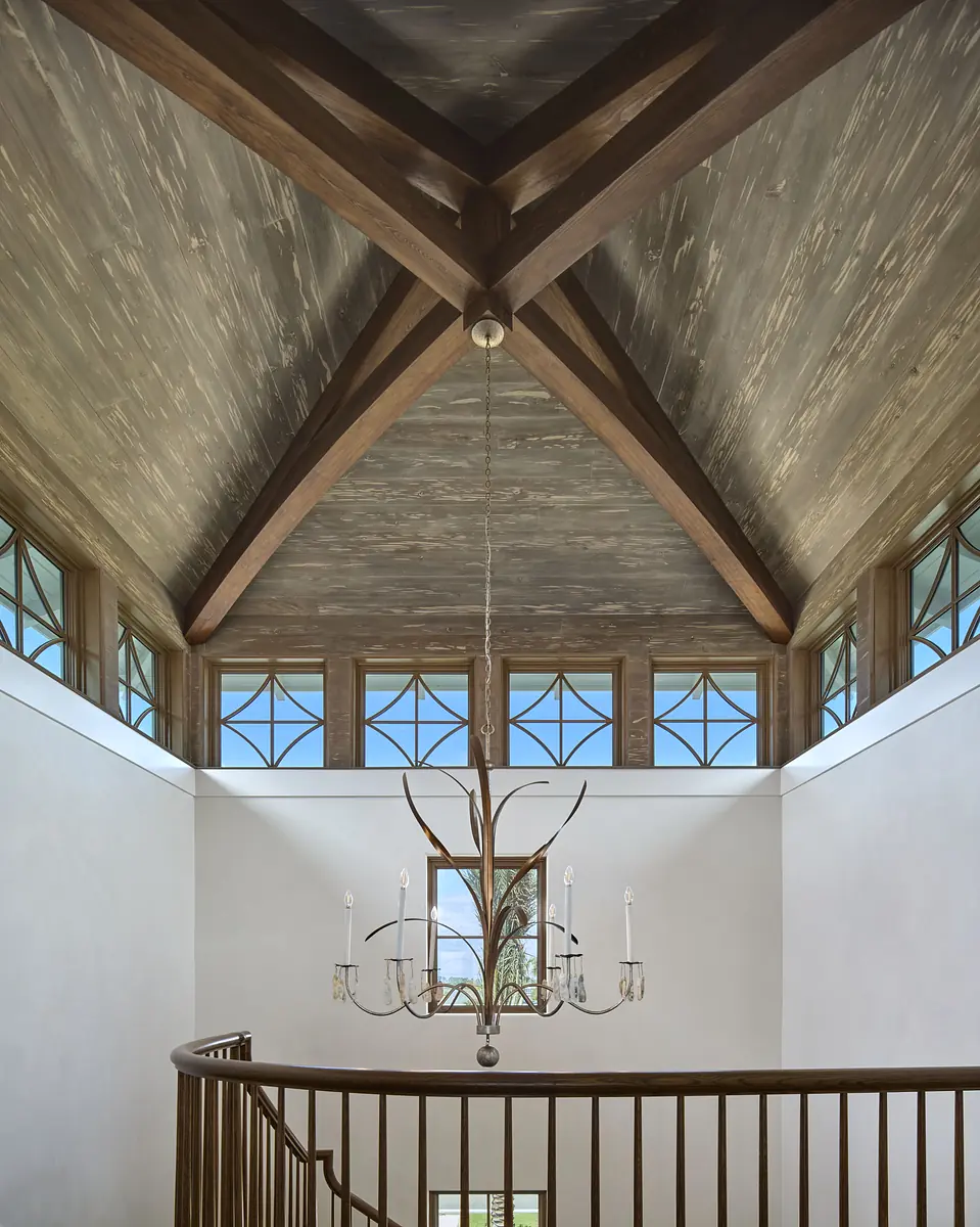 Hallway with wooden railing, large windows, vaulted ceiling, exposed beams, and chandelier.