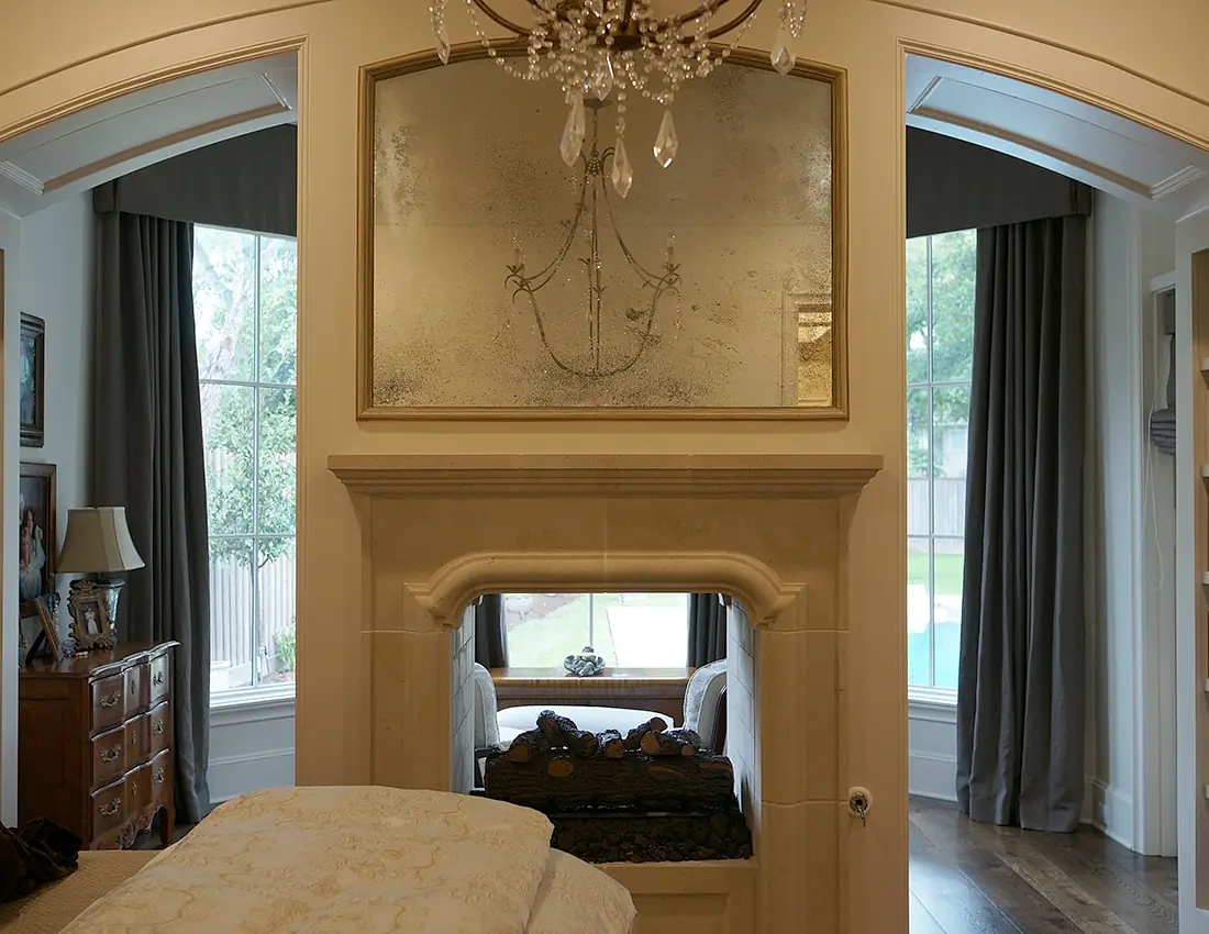 Bedroom with bed, quilt, pillows, wooden dresser, fireplace, windows, and mirror.