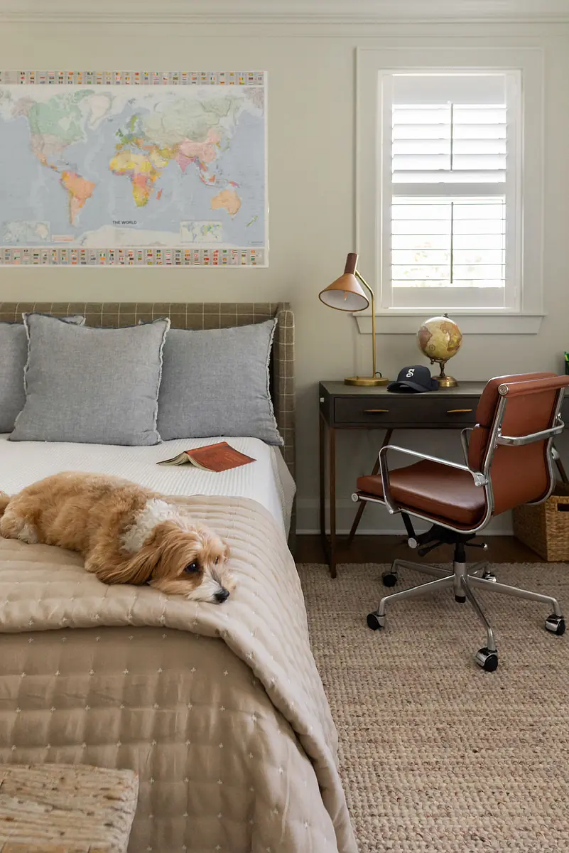 Bedroom with bed, desk, globe, world map on the wall, and a dog resting on the quilt