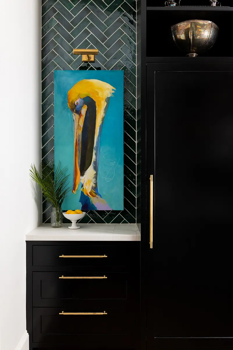 Small area with black cabinetry, marble countertop, herringbone tile, pelican painting, and fruit bowl.