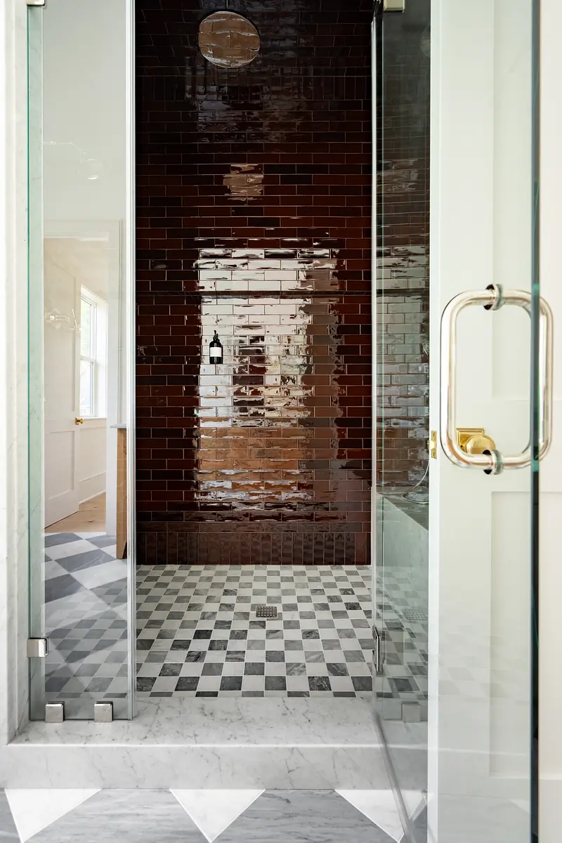 Bathroom with glass shower, checkerboard floor, red subway tiles, and marble accents.