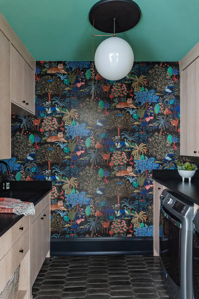 Small kitchen area with dark cabinetry, black countertop, tropical wallpaper, and hexagonal tiles.