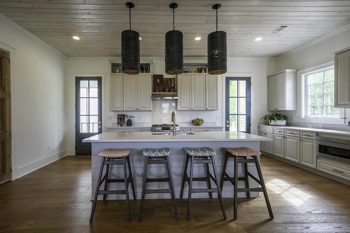 Kitchen with large island, stools, white cabinetry, stainless steel stove, hardwood floor, and natural light from windows