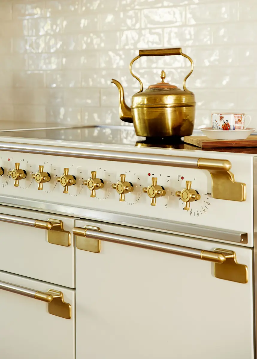 Kitchen with professional stove, gold knobs, white tiled backsplash, and kettle.
