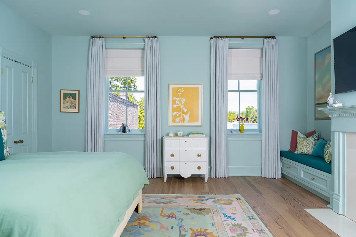 Bedroom with teal wall, green bedspread, windows, white dresser, and floral area rug.