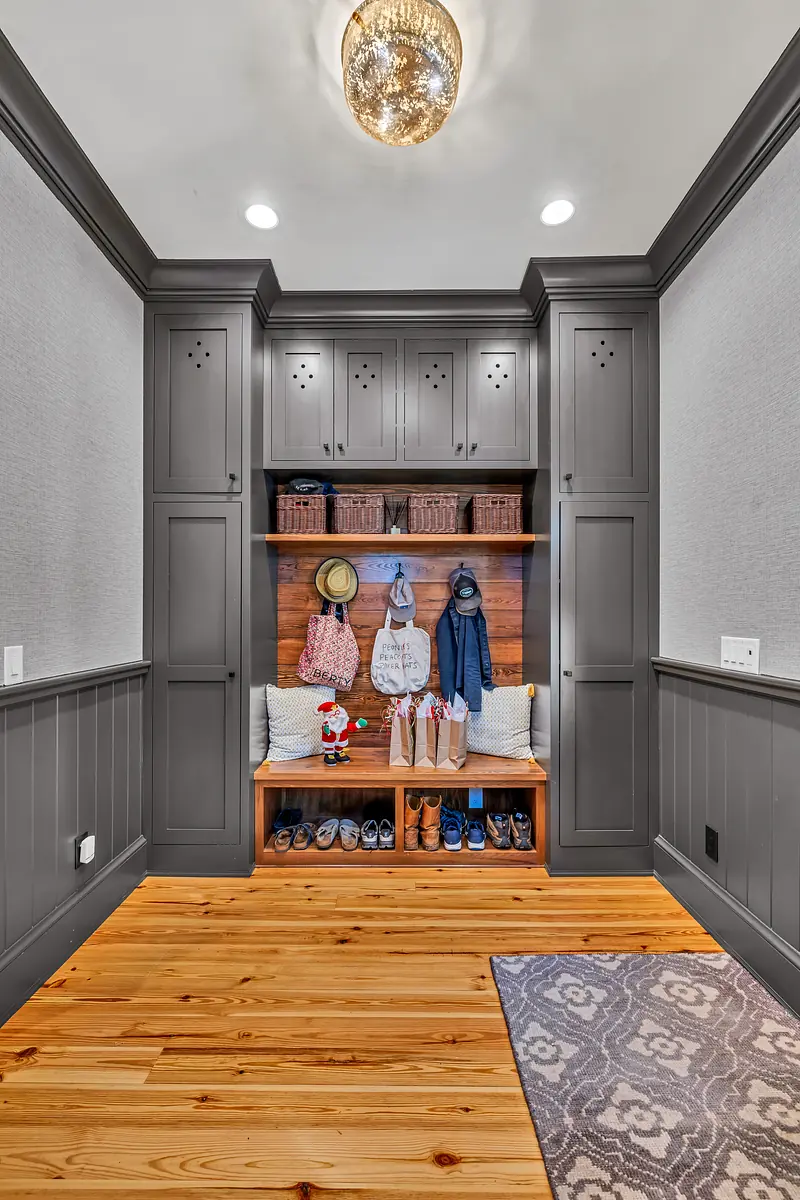 Mudroom with built-in bench, gray cabinetry, wall hooks, and patterned area rug on wooden floor