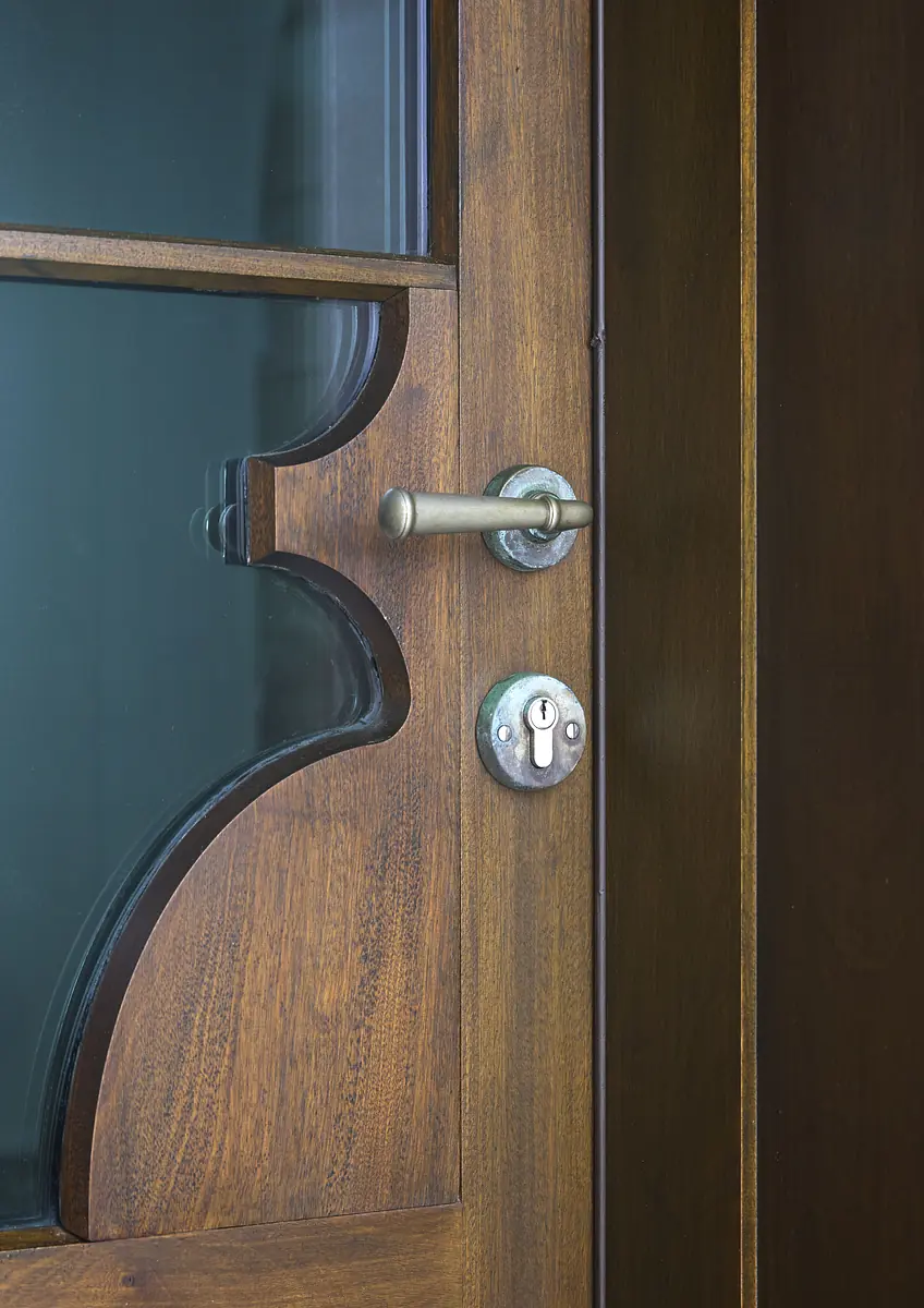 Close-up of a decorative wooden door with glass panel, handle, and lock.
