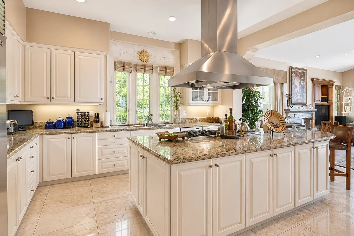 Kitchen with white cabinetry, granite island, stainless steel appliances, and a dining area in the background.