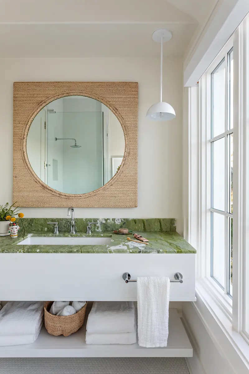 Bathroom with white vanity, green countertop, round mirror, and natural light from a window