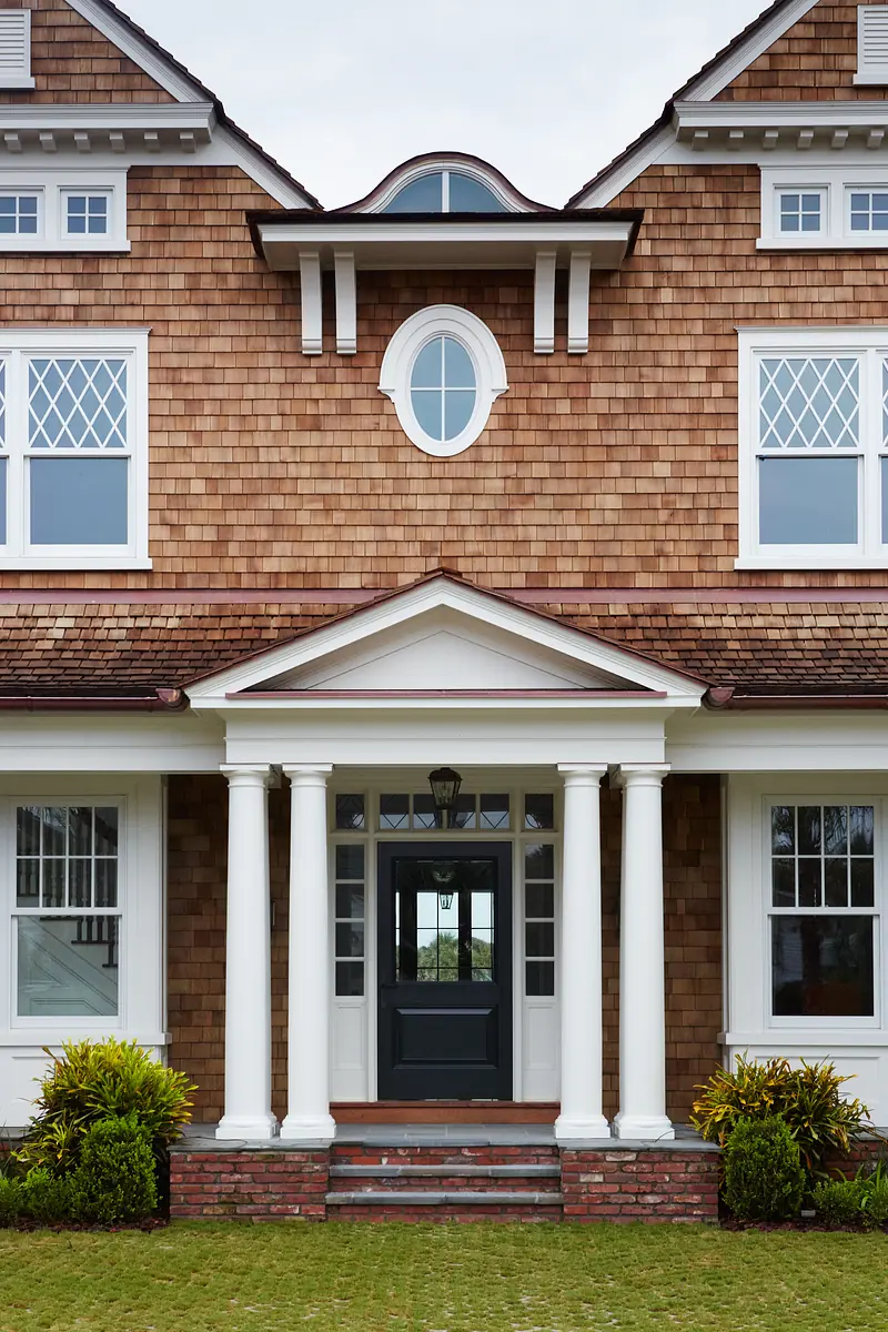 Exterior front with columns, dark door, wooden shingles, windows with shutters, and round window above.