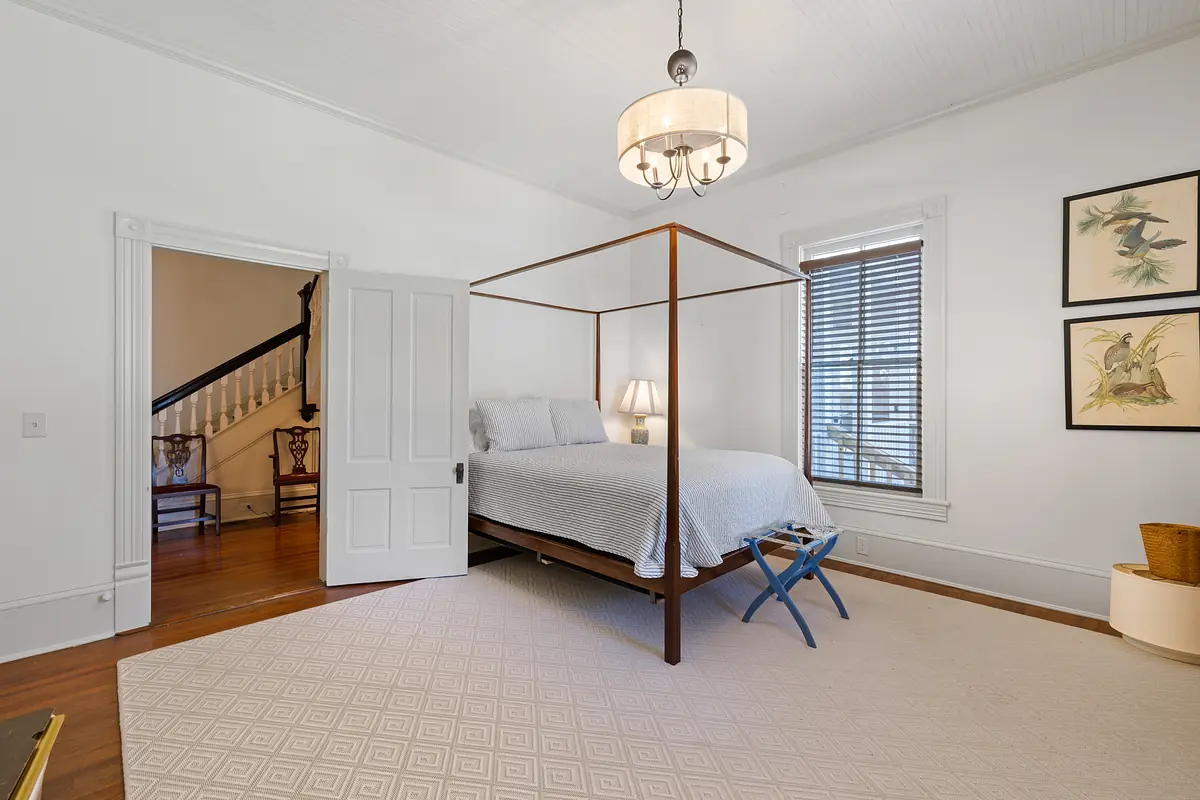 Bedroom with four-poster bed, gray quilt, lamps, artwork, and area rug.