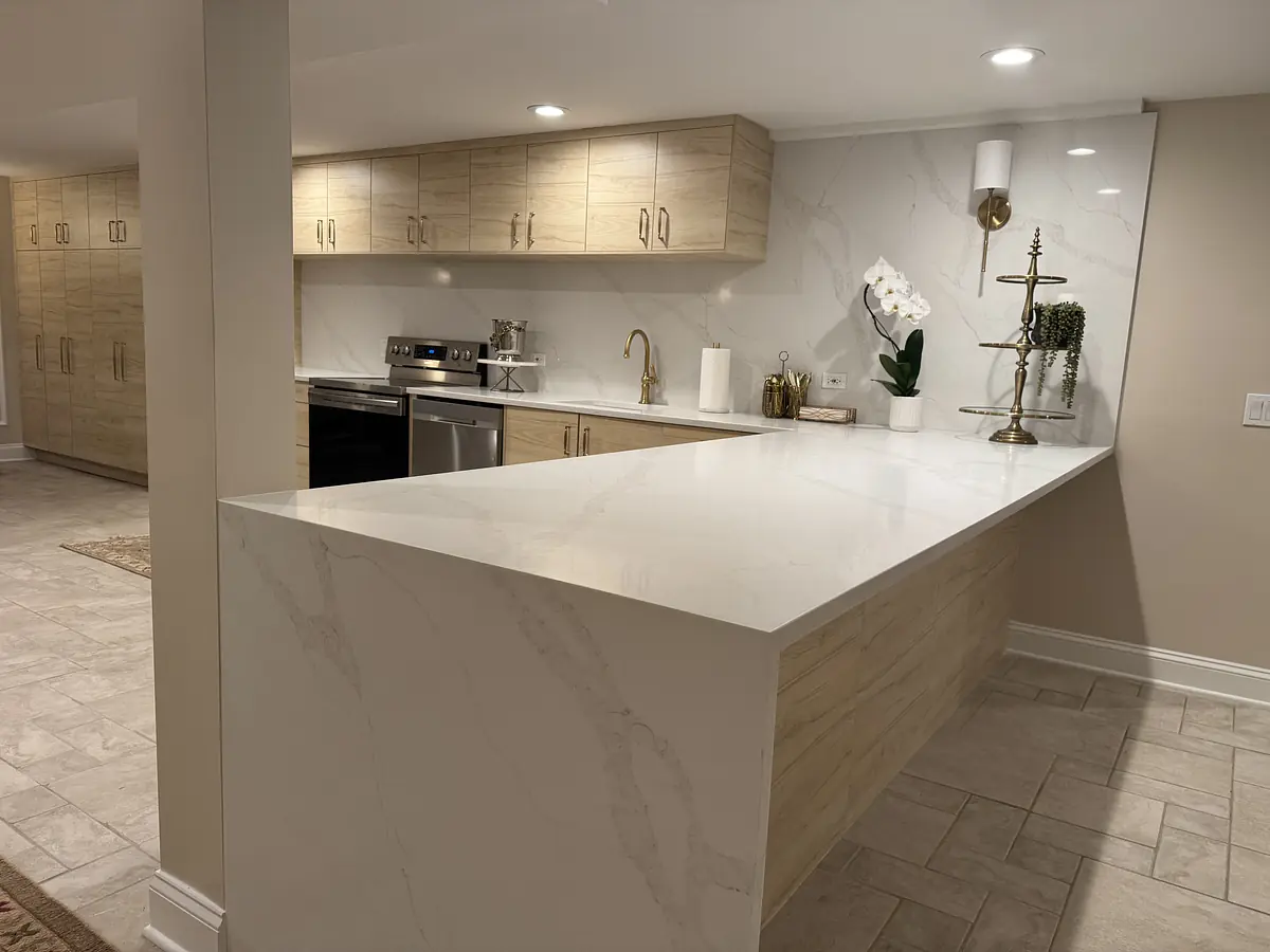 Kitchen with light wood cabinetry, large white marble island, stainless steel appliances, and a wall sconce.