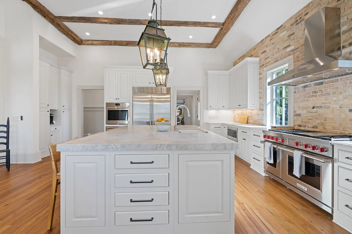 Kitchen with marble island, white cabinets, stainless steel appliances, and exposed brick wall.