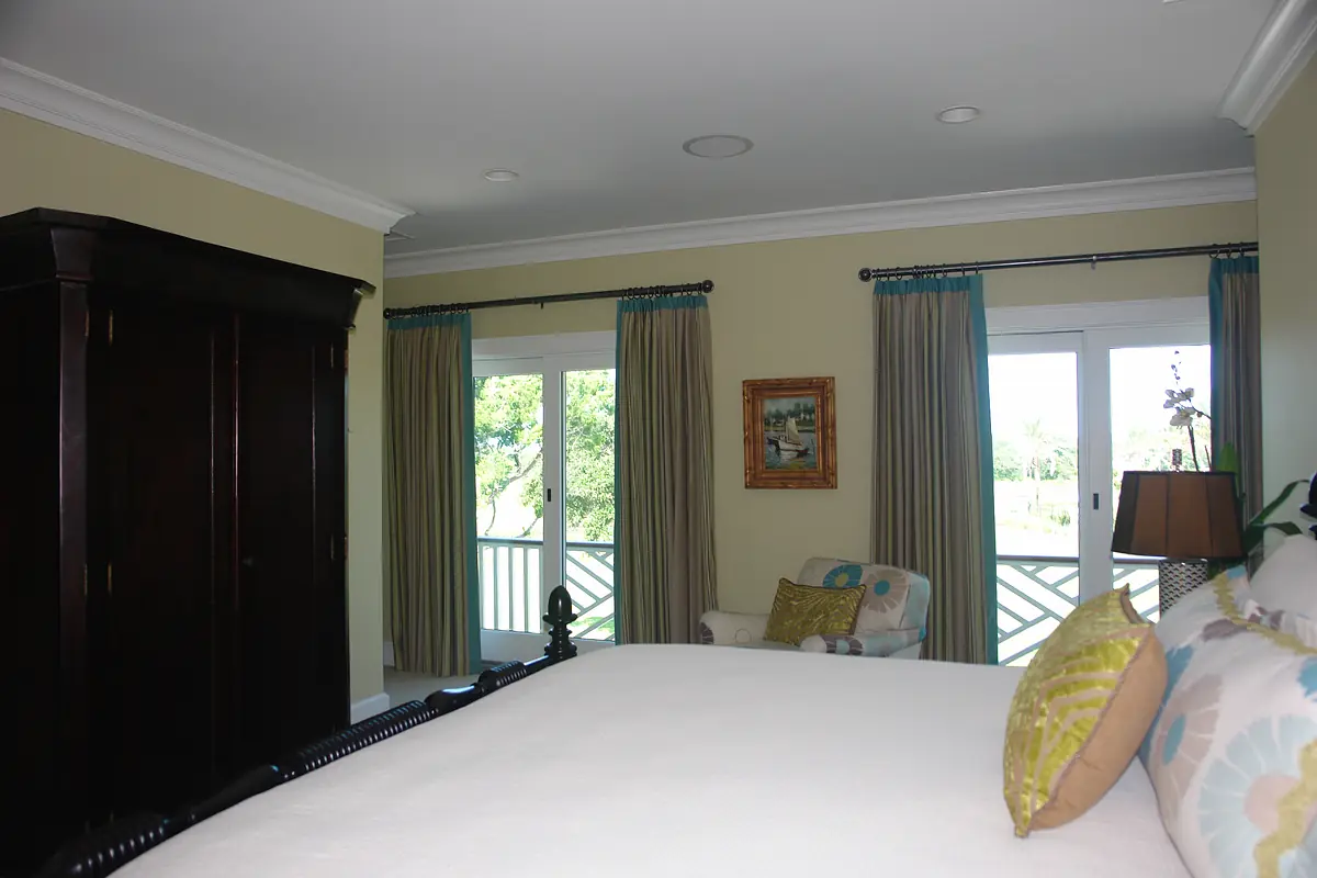 Bedroom with large bed, upholstered chair, armoire, large windows, and framed painting.