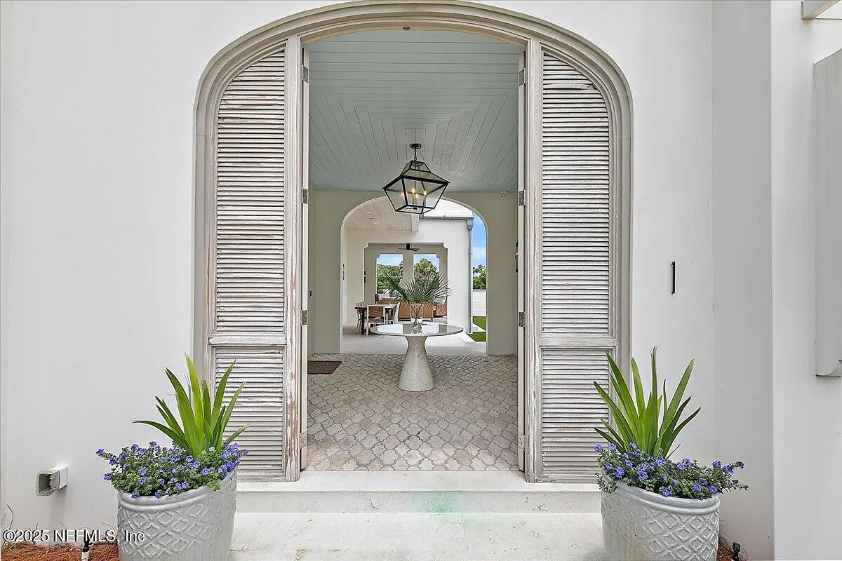 Foyer with arched doors, pendant light, planters, cobblestone floor, and panel ceiling leading to an open area.