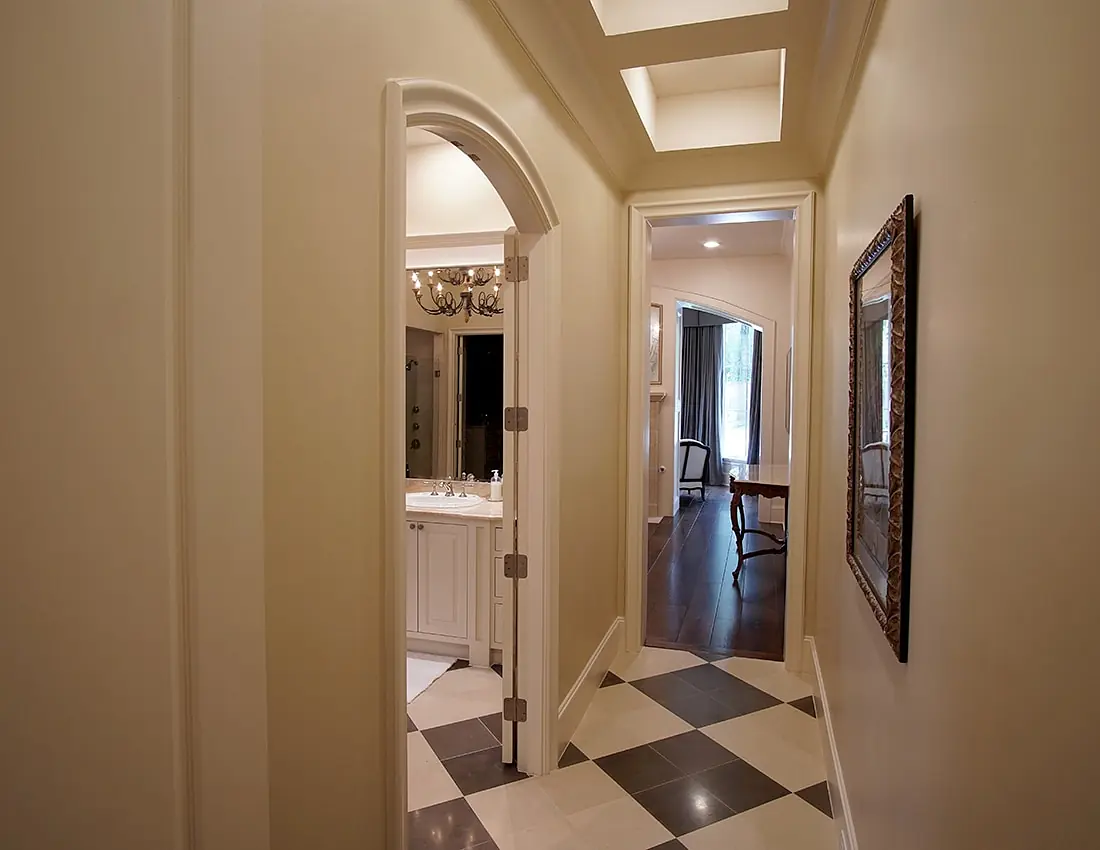 Hallway with cream walls, black and white tile floor, and two doorways leading to a bathroom and another room.