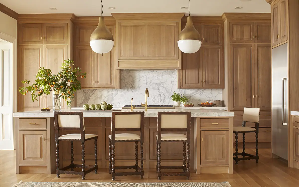 Kitchen with wooden cabinets, marble backsplash, island with bar stools, and stainless steel refrigerator