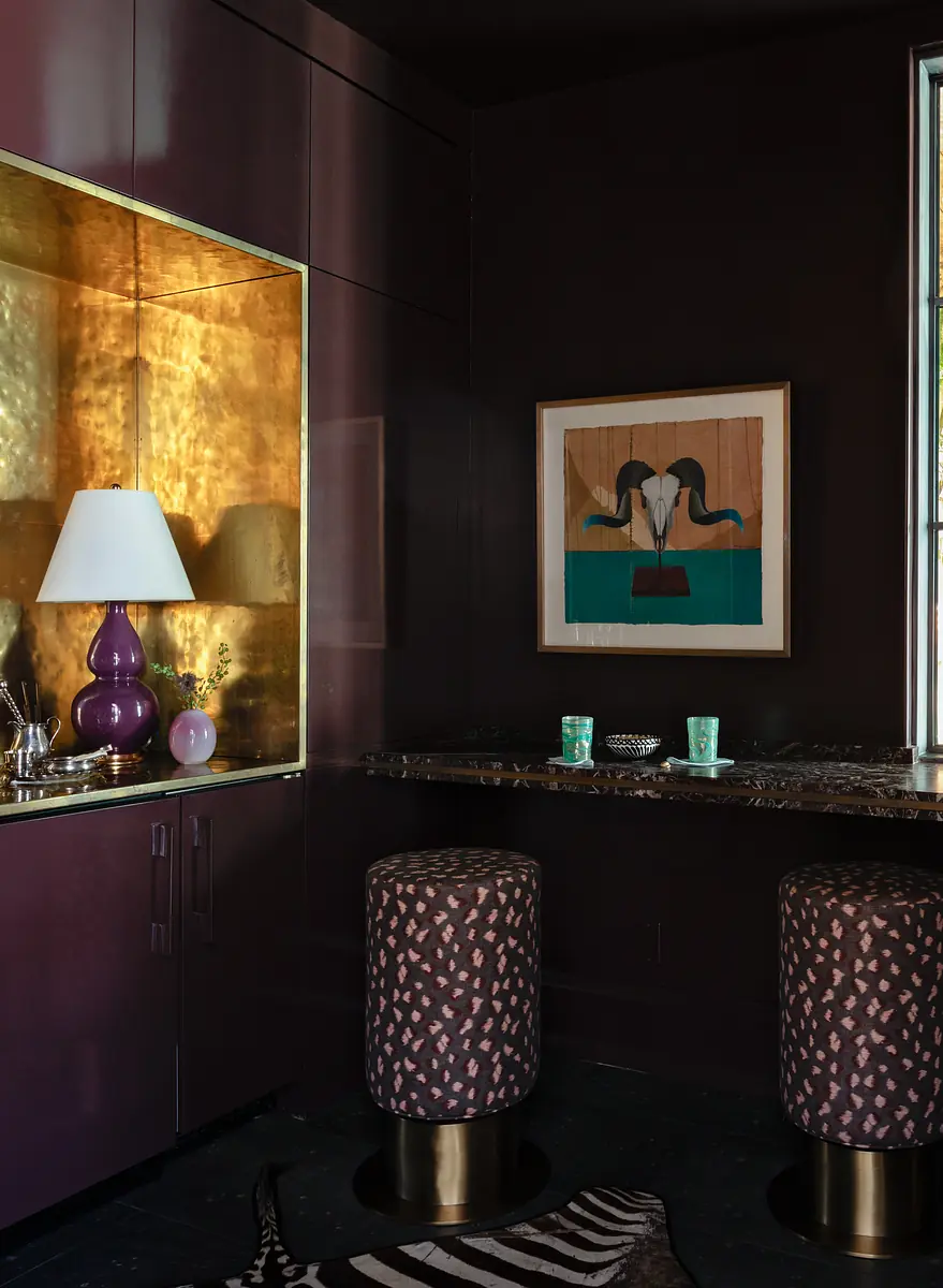 Corner with gold accent wall, marble countertop, two stools, purple lamp, and framed artwork.