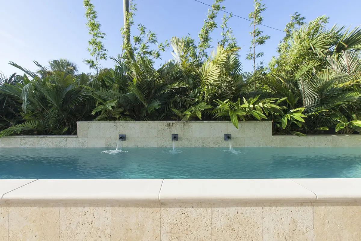 Outdoor space with rectangular pool, three water features, and tropical plants surrounding it