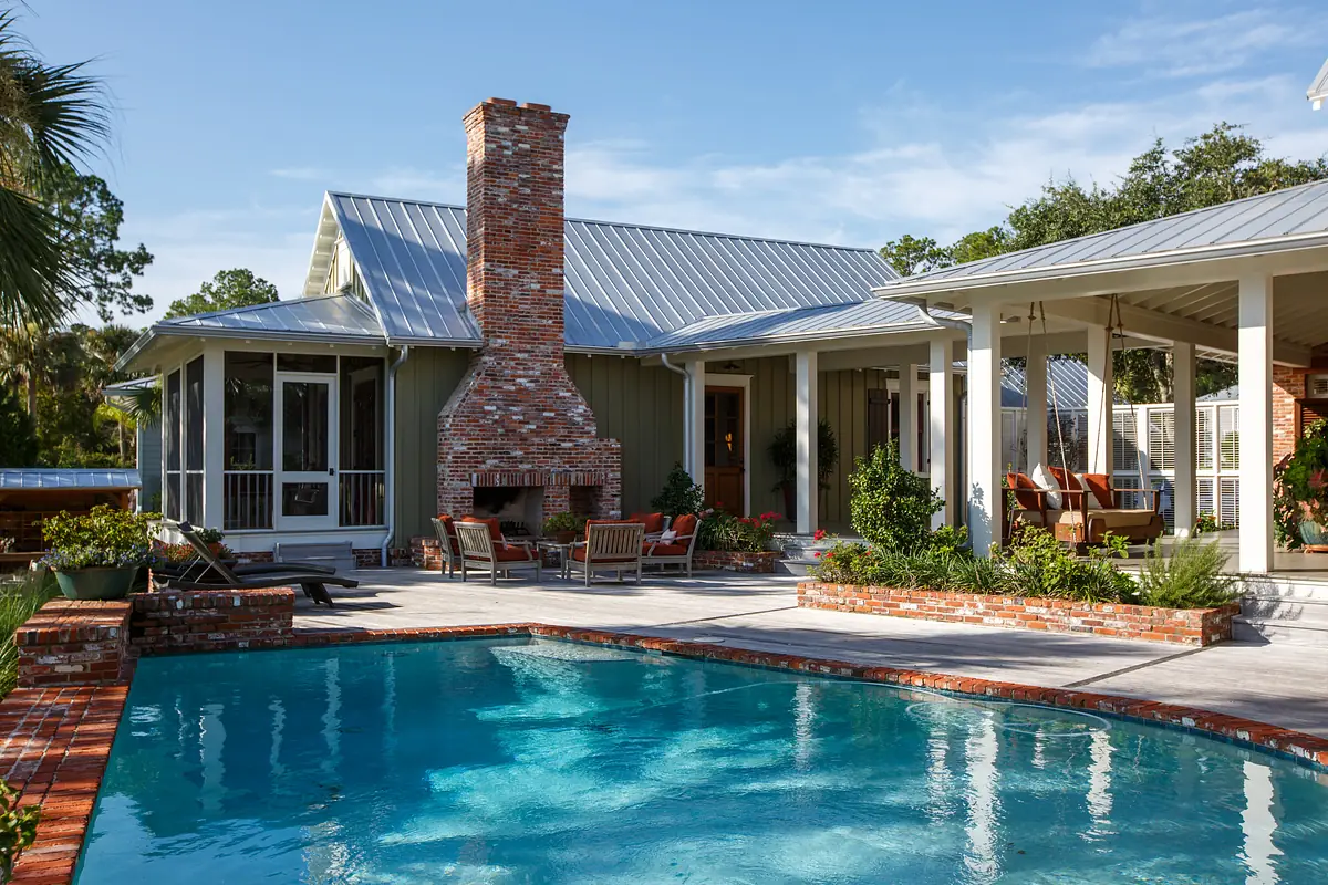 Exterior rear view with pool, brick patio, fireplace, seating areas, and greenery