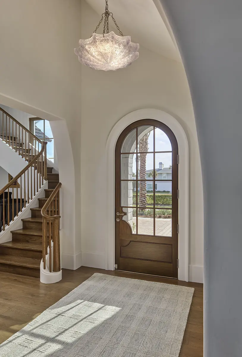 Foyer with curved staircase, arched wooden door, area rug, and white walls.