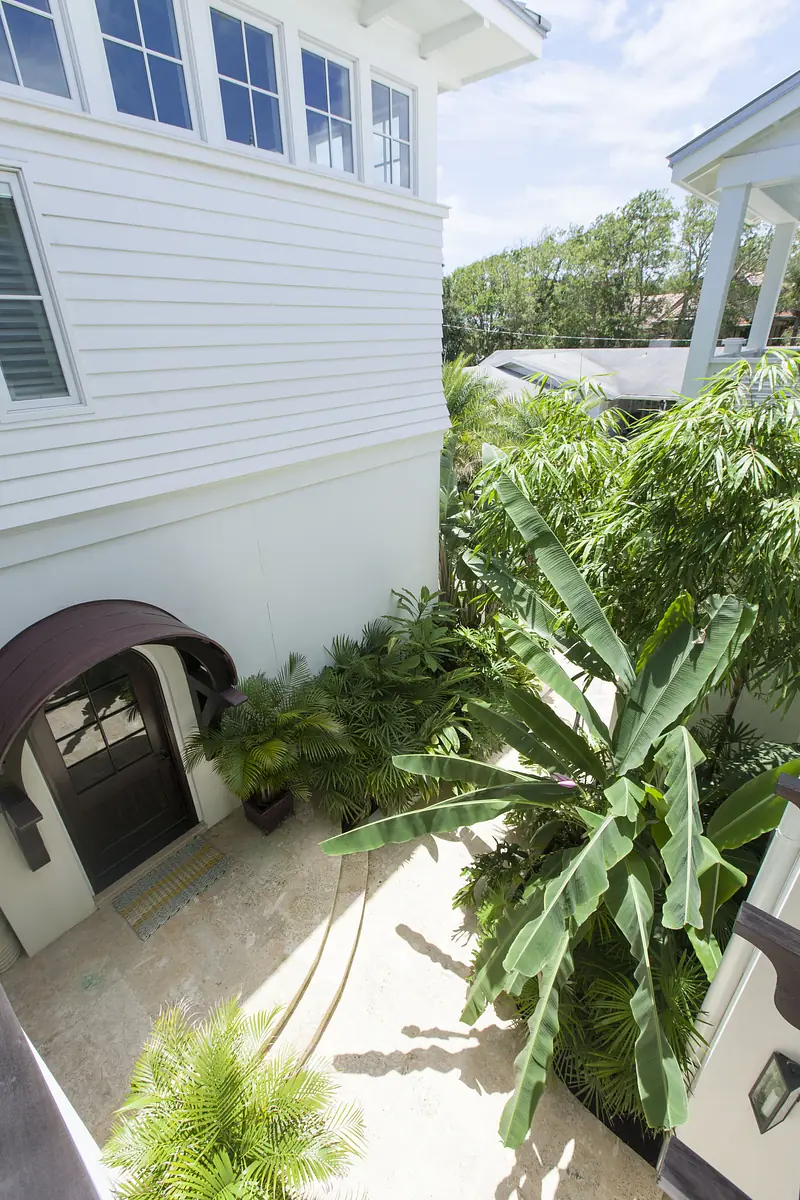 Exterior front view with tropical plants, a curved entryway, white siding, large windows, and a pathway.