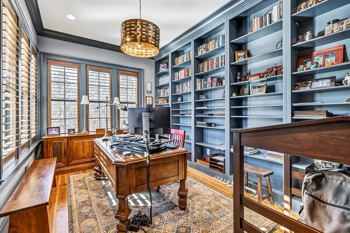 Office with wooden desk, computer, bookshelves, two windows, and patterned area rug.
