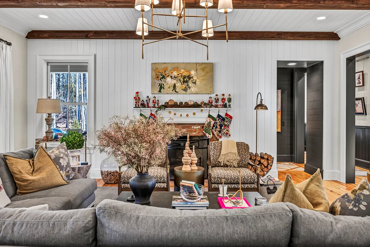 Living room with gray sofa, wooden coffee table, area rug, fireplace, decorative painting, and plants