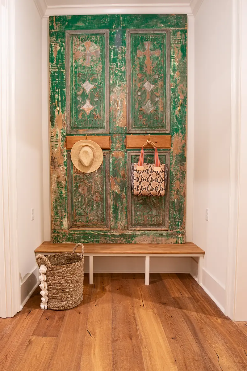 Mudroom with wooden bench, vintage door, straw hat, bag, and woven basket on hardwood floor.