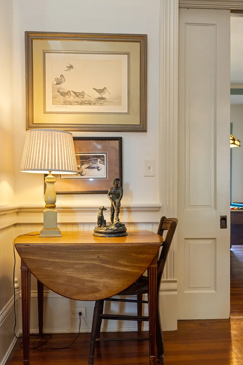 Small space with drop-leaf table, wooden chair, lamp, art, and sculpture.