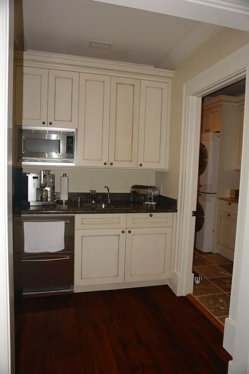 Compact kitchen with beige cabinetry, stainless steel appliances, dark granite countertop, and hardwood flooring.